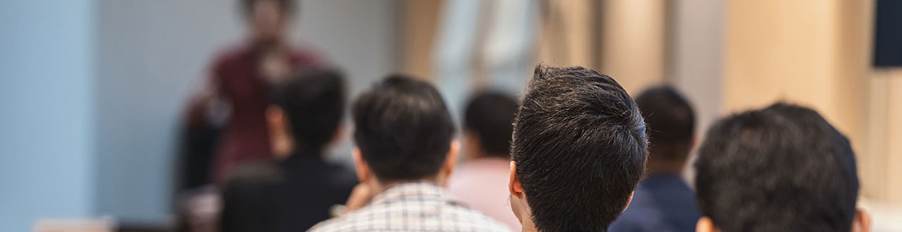 Titelbild Trainer Menschen horchen gespannt einem Dozenten in einem Seminarraum